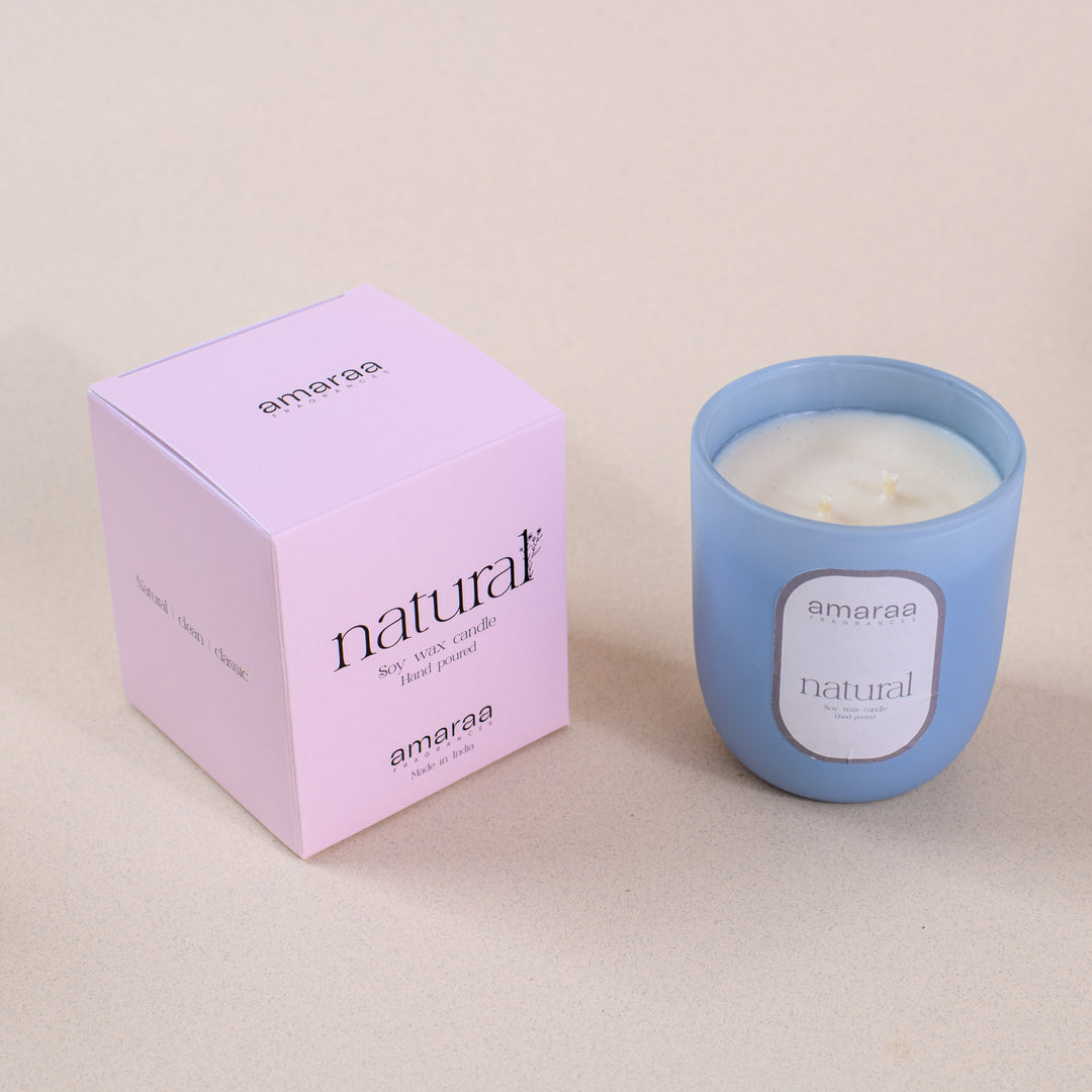 Amaraa natural soy wax candle in blue glass with pink box on beige surface