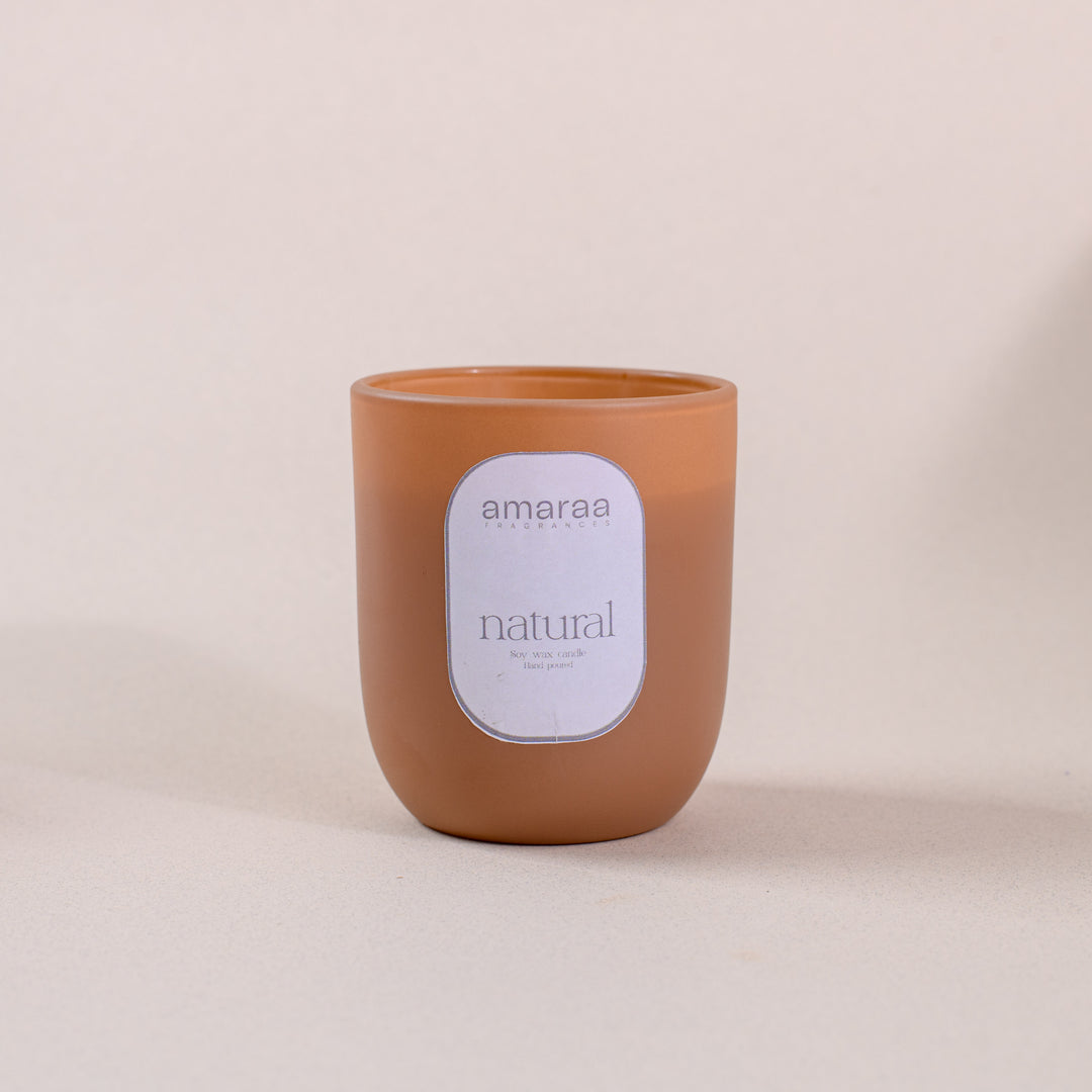 Brown amaraa natural soy wax candle with label on neutral background