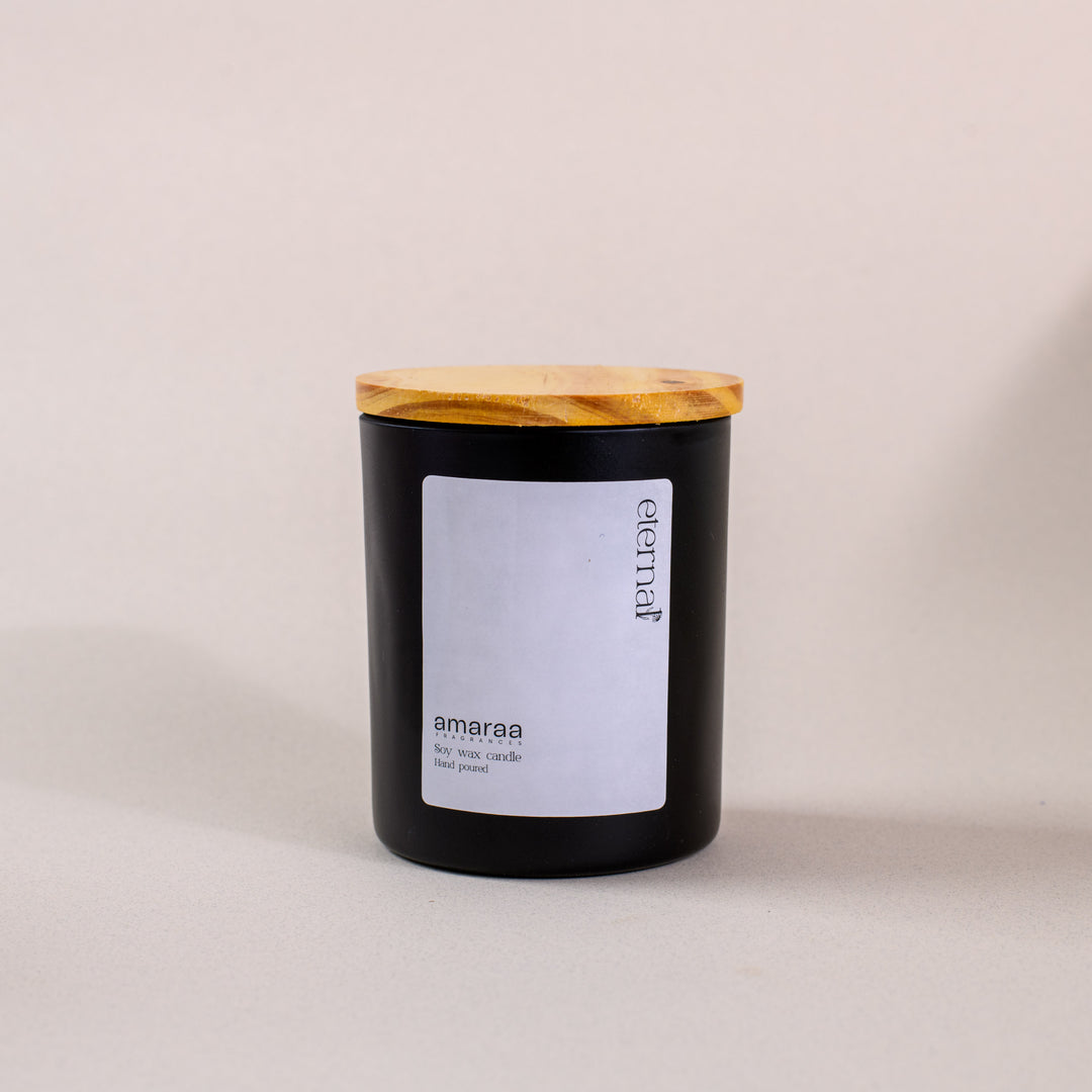 Black amaraa soy wax candle with wooden lid and white label on neutral background
