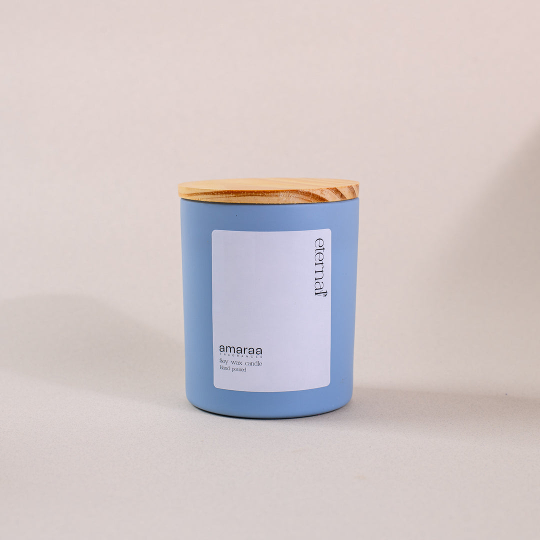 Blue soy wax candle with wooden lid and white label on neutral background