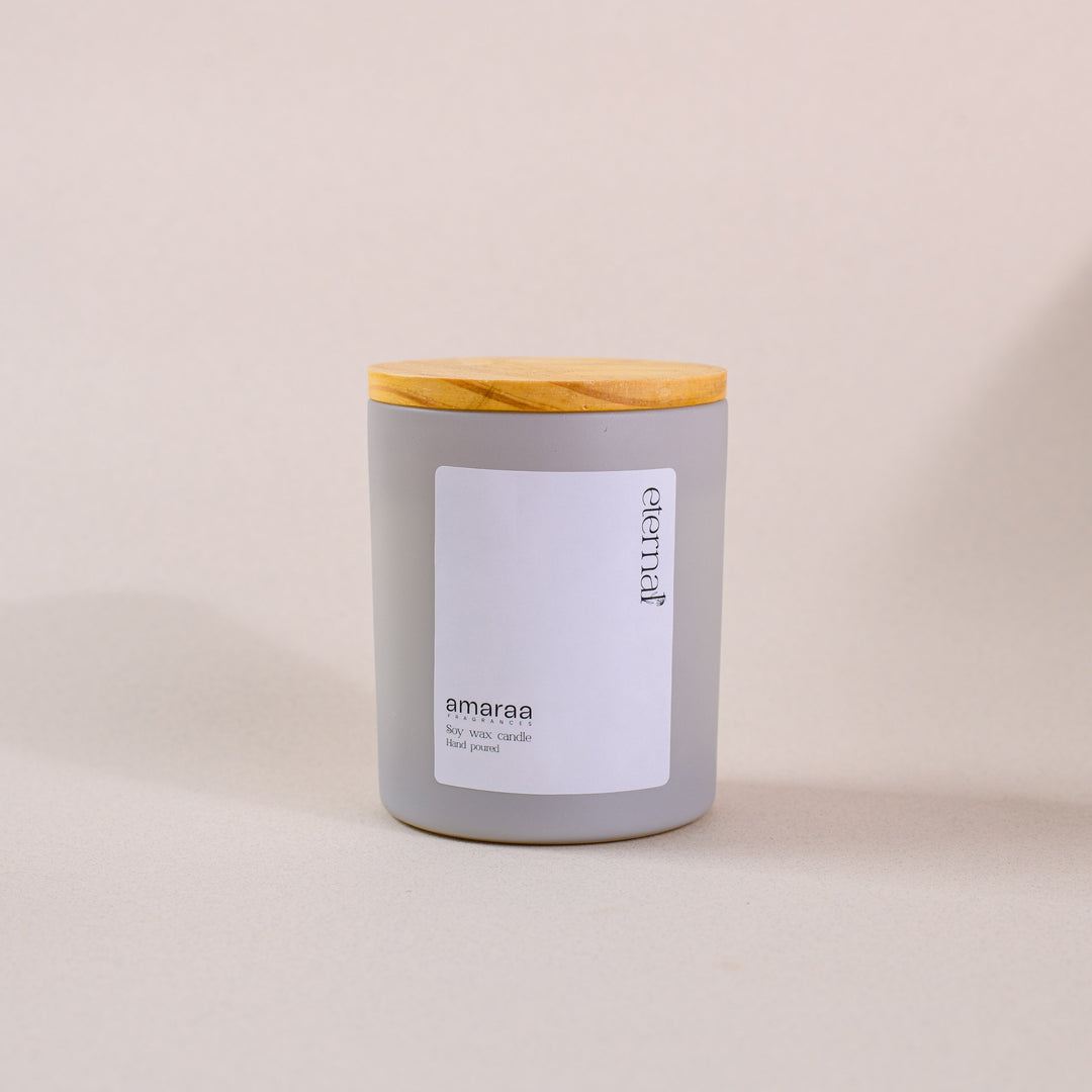 Gray glass soy wax candle with wooden lid on neutral background, labeled 'eternal amaraa'.