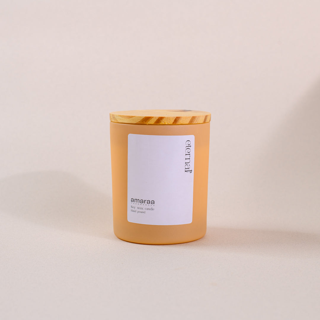Amber glass soy wax candle with wood lid and 'eternal amaraa' label on beige background