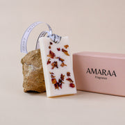 AMARAA fragrance wax tablet with dried flowers beside pink box and stone on beige background