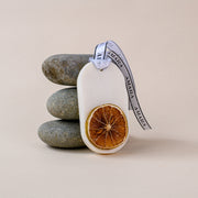 Scented wax tablet with dried orange slice and branded ribbon, stacked stones background