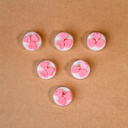 Six white tealight candles with pink heart shapes on brown background