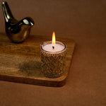 Load image into Gallery viewer, Decorative gold candle holder with lit candle on wooden tray, metallic bird figurine in background