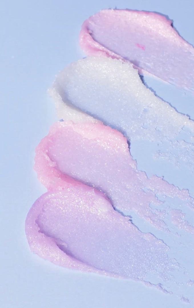 Pink and purple shimmery lip scrub swatches on a pale blue background