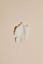 Load image into Gallery viewer, Close-up of a damaged drywall with a hole on a beige painted wall surface