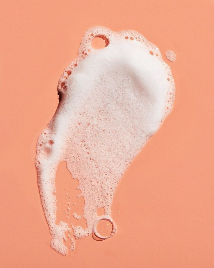 White soap foam with bubbles on a peach background, skincare product texture