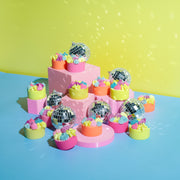 Colorful mini cakes with rainbow frosting and disco balls on pink platforms, pastel background