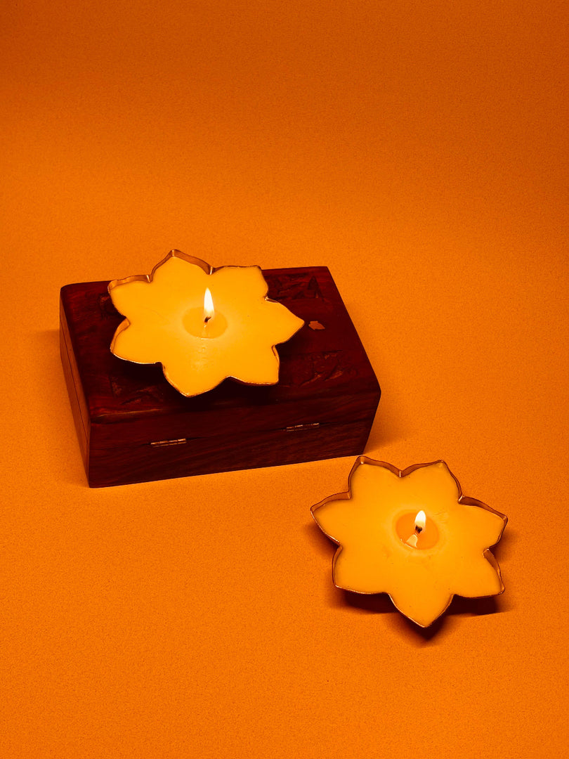 Flower-shaped yellow candles on a wooden box and orange background, festive decor