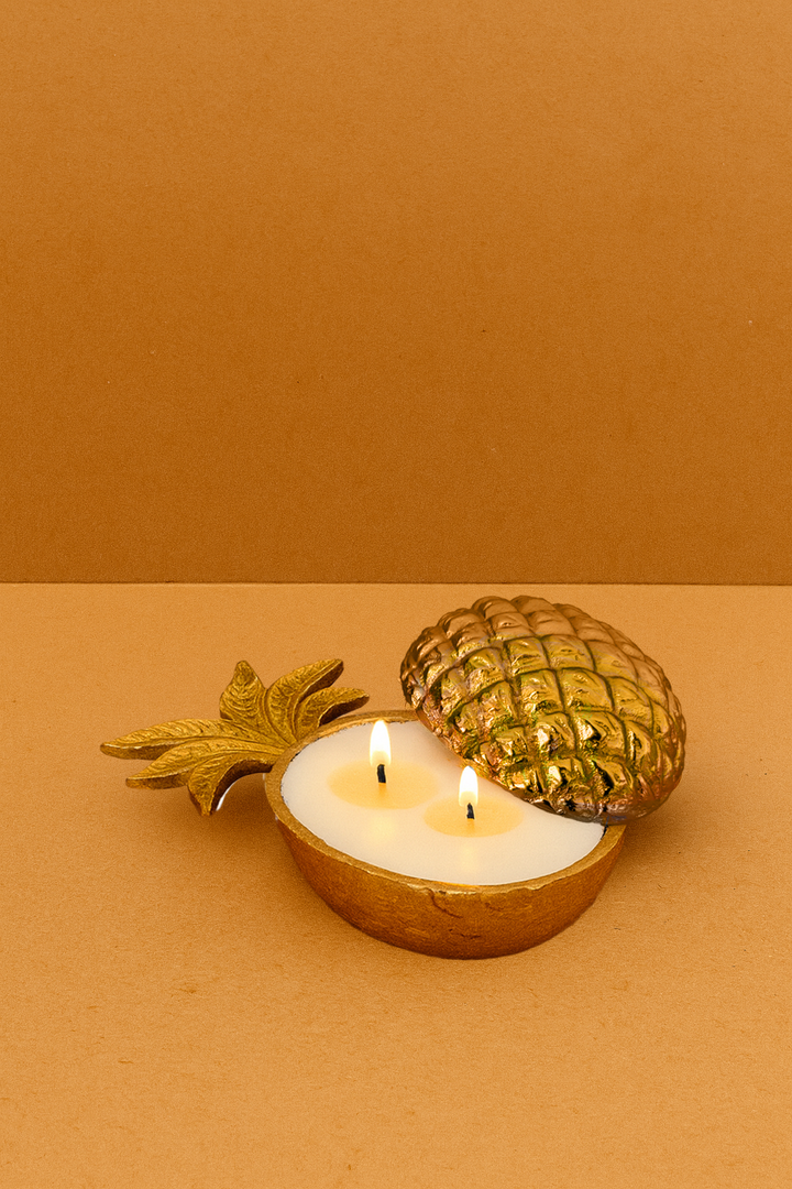 Gold pineapple-shaped candle holder with two lit candles on a brown background